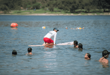 Instructor in red shorts and lifeguard shirt teaching waterfront lifeguard certification course on a lake with students in water. Ideal for lake safety training.