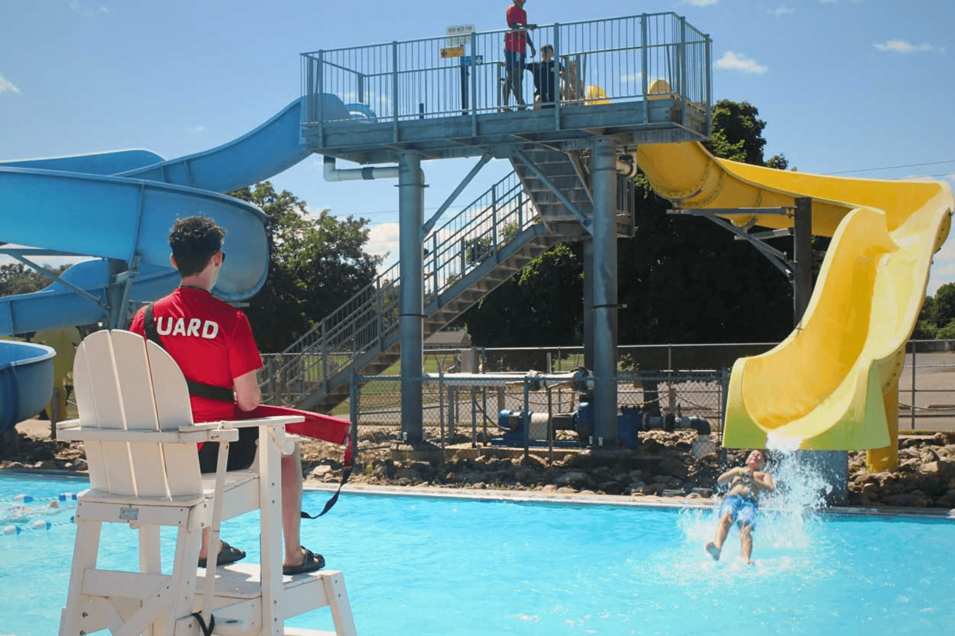 Waterpark Lifeguard Certification Course showing a lifeguard supervising a water slide pool area with a trainee sliding into the water. Ideal for lifeguard training in recreational water safety.