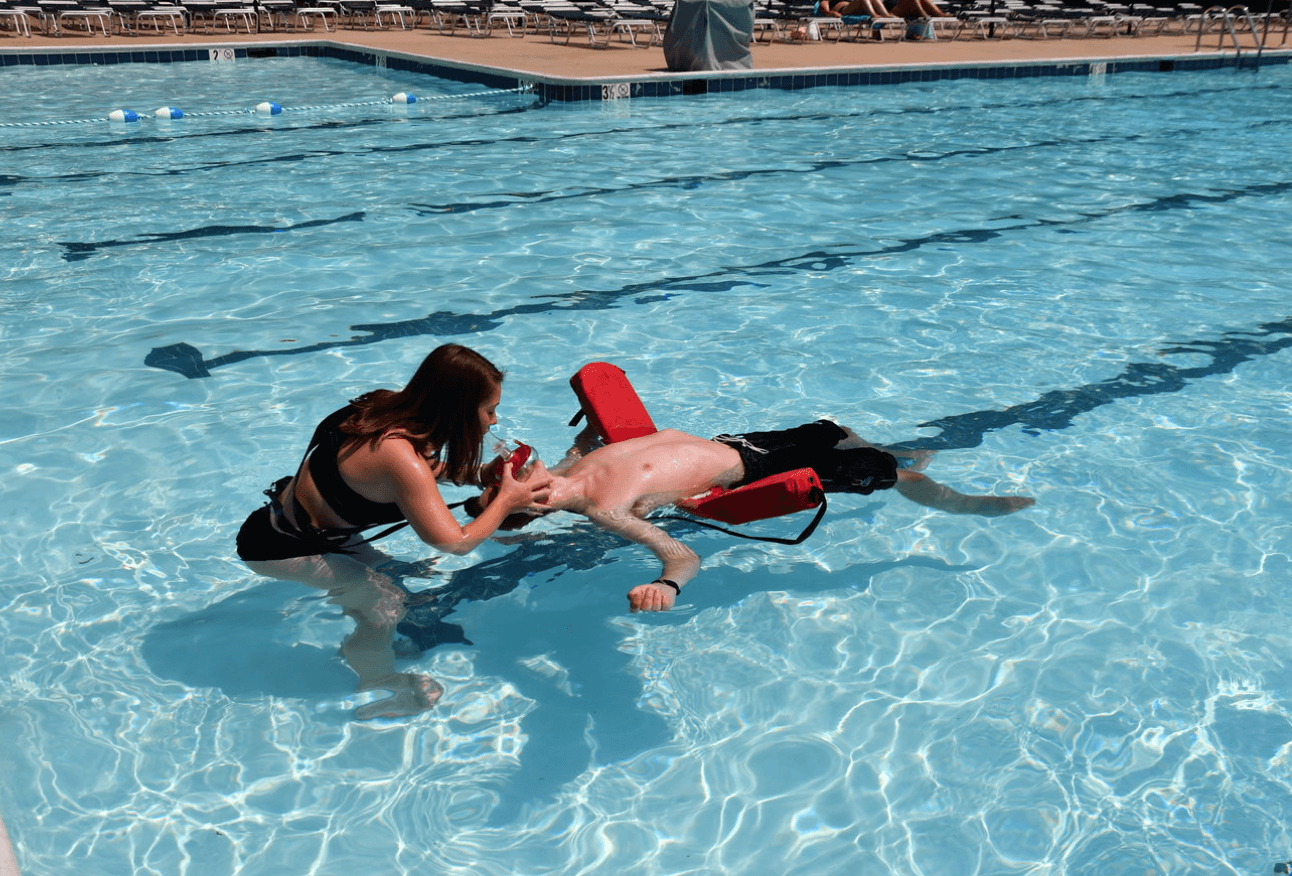 Trainee performs rescue breathing on a manikin during Shallow Pool Lifeguard Certification in a pool under 5 feet deep. Course focuses on emergency response skills.