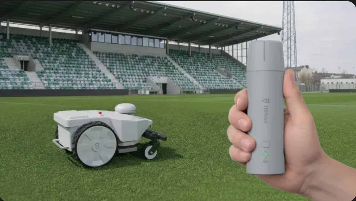 Hand holding remote control for robotic mower on sports field